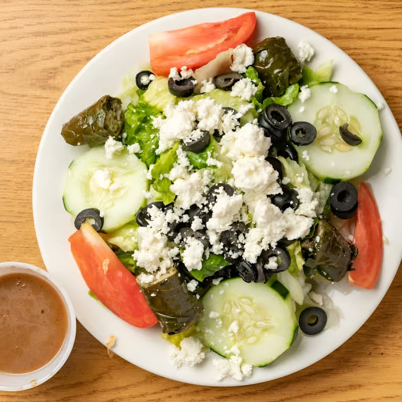 A Marinelli's Pizza Greek salad with lettuce, tomatoes, cucumbers, olives, feta, and stuffed grape leaves.