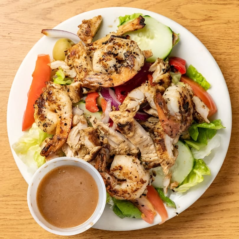 Grilled chicken and shrimp salad with lettuce, tomatoes, cucumbers, olives, and dressing.
