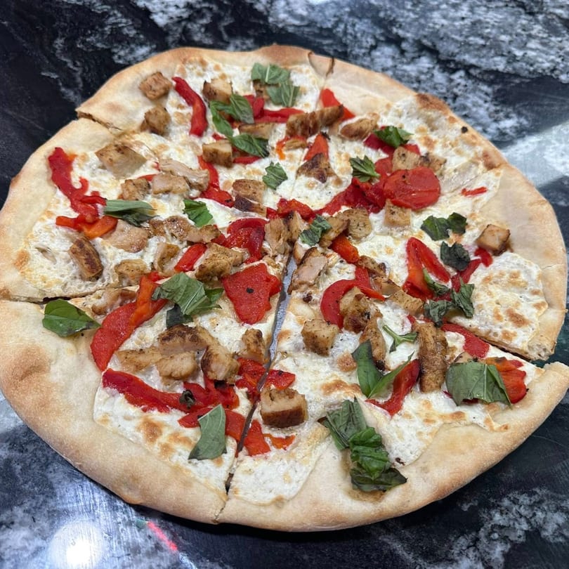 Marinelli's white pizza with chicken, roasted red peppers, and fresh basil on a dark countertop.