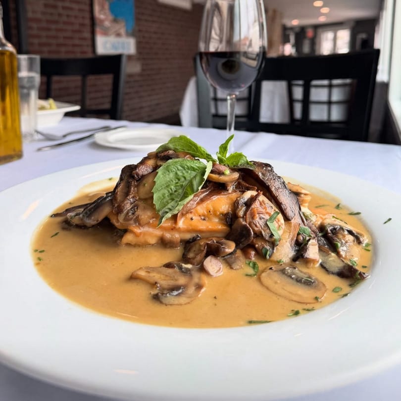 Chicken dish with mushrooms and creamy sauce, garnished with basil, on a white plate with red wine.